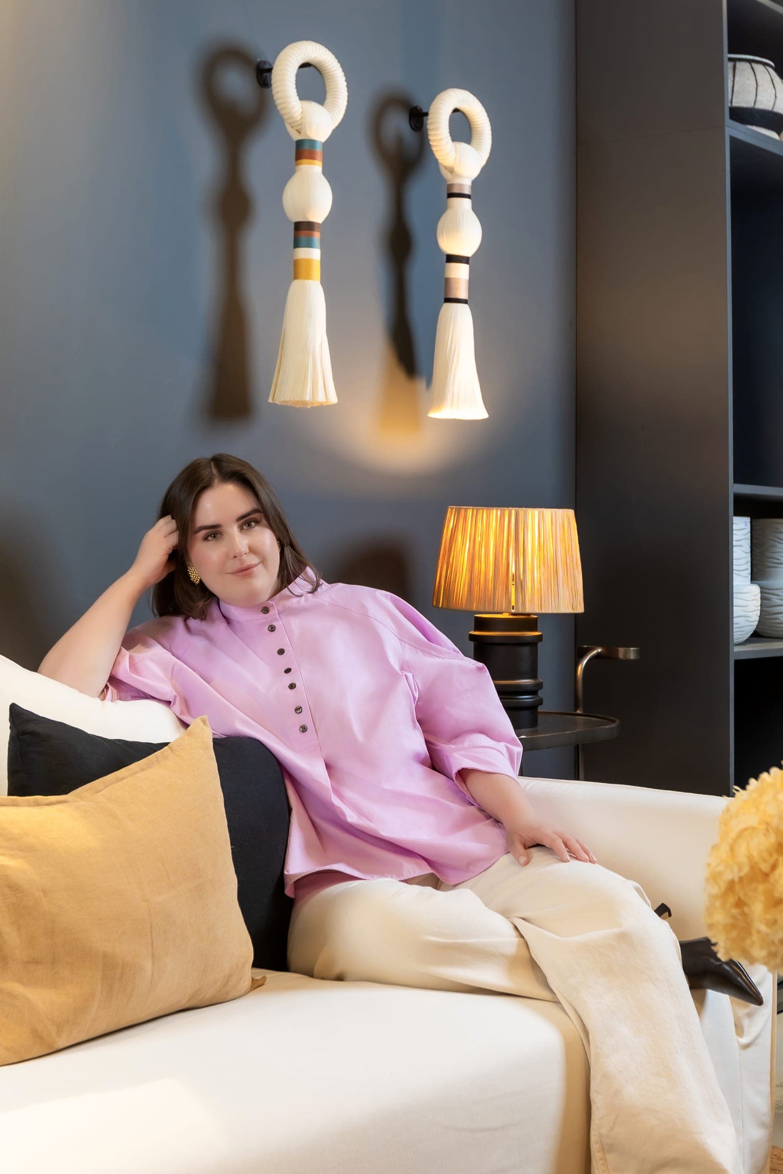 Emilie on a cream sofa beneath tasselled wall hangings