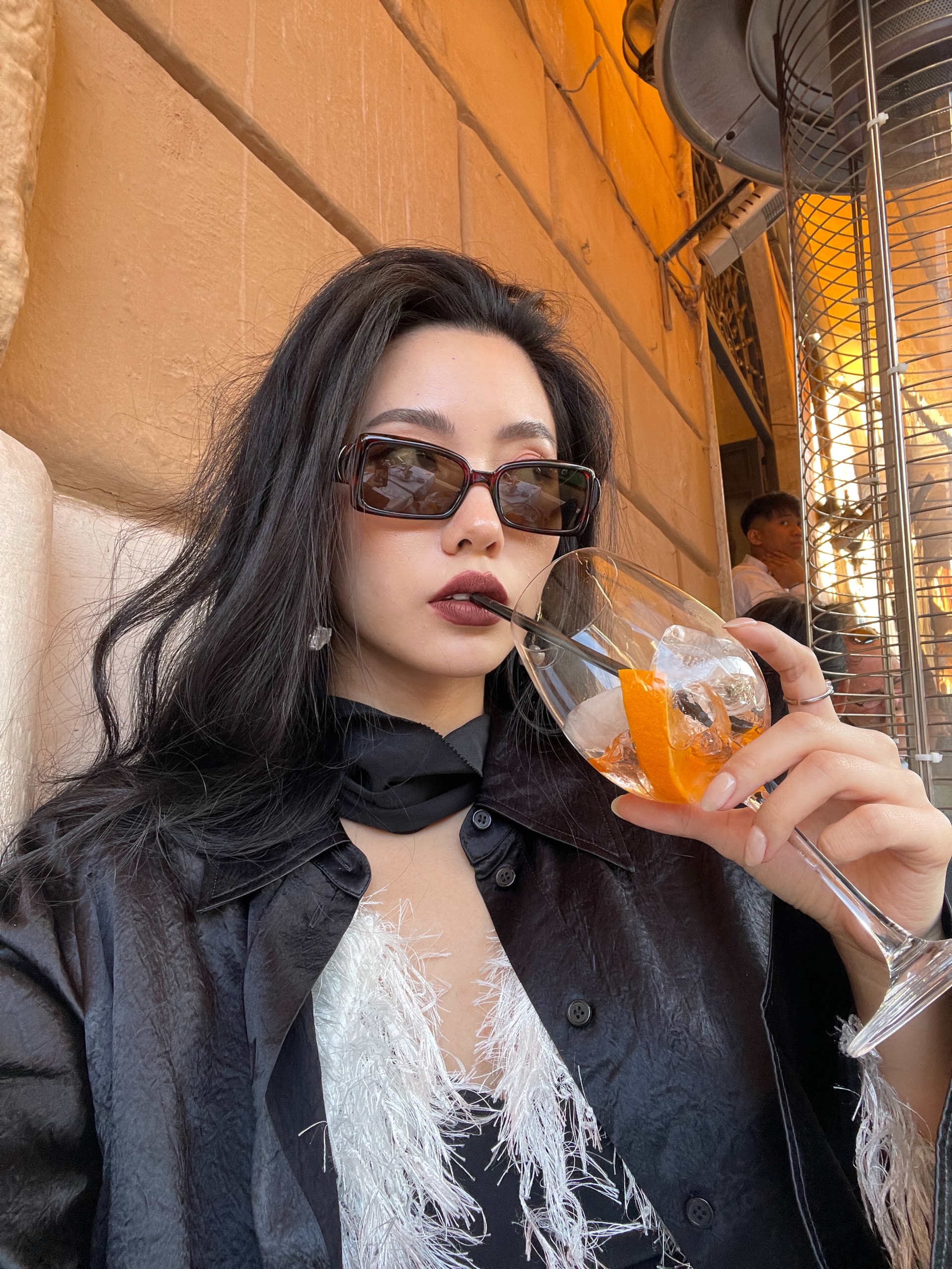 Vailey sipping a spritz against an ochre wall