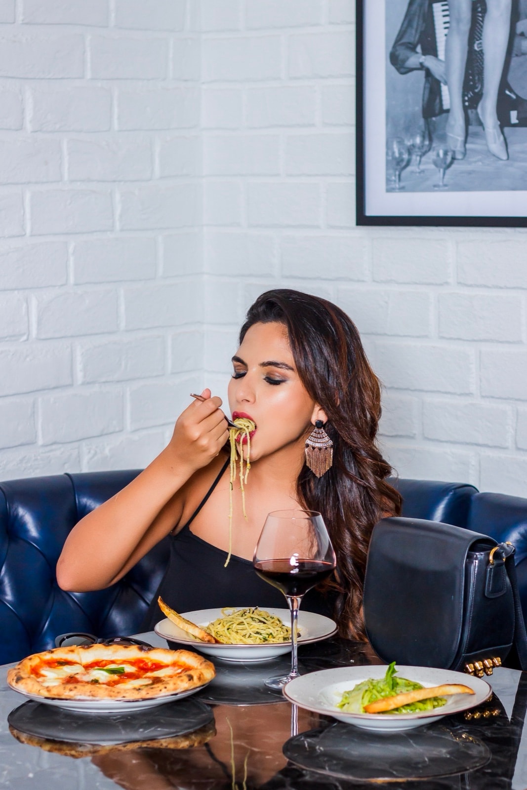 Karishma mid-pasta against a white brick wall