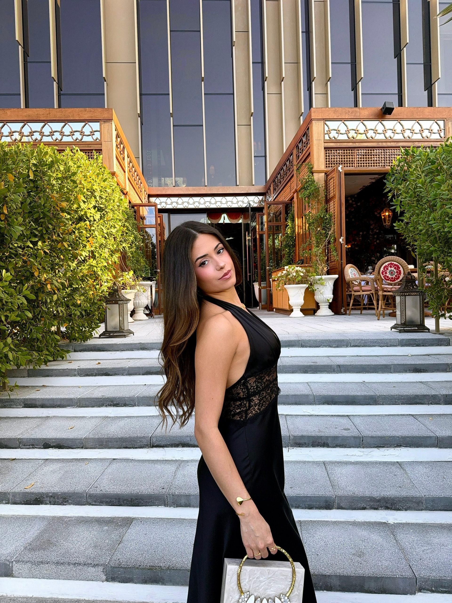 Letty on the steps of a golden hotel facade in a black dress