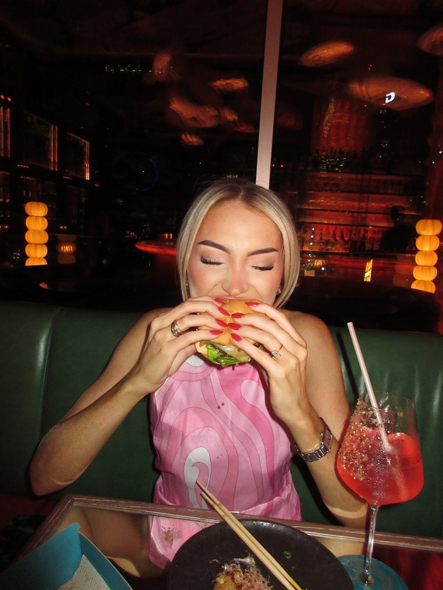 Orla biting into a burger on a green banquette