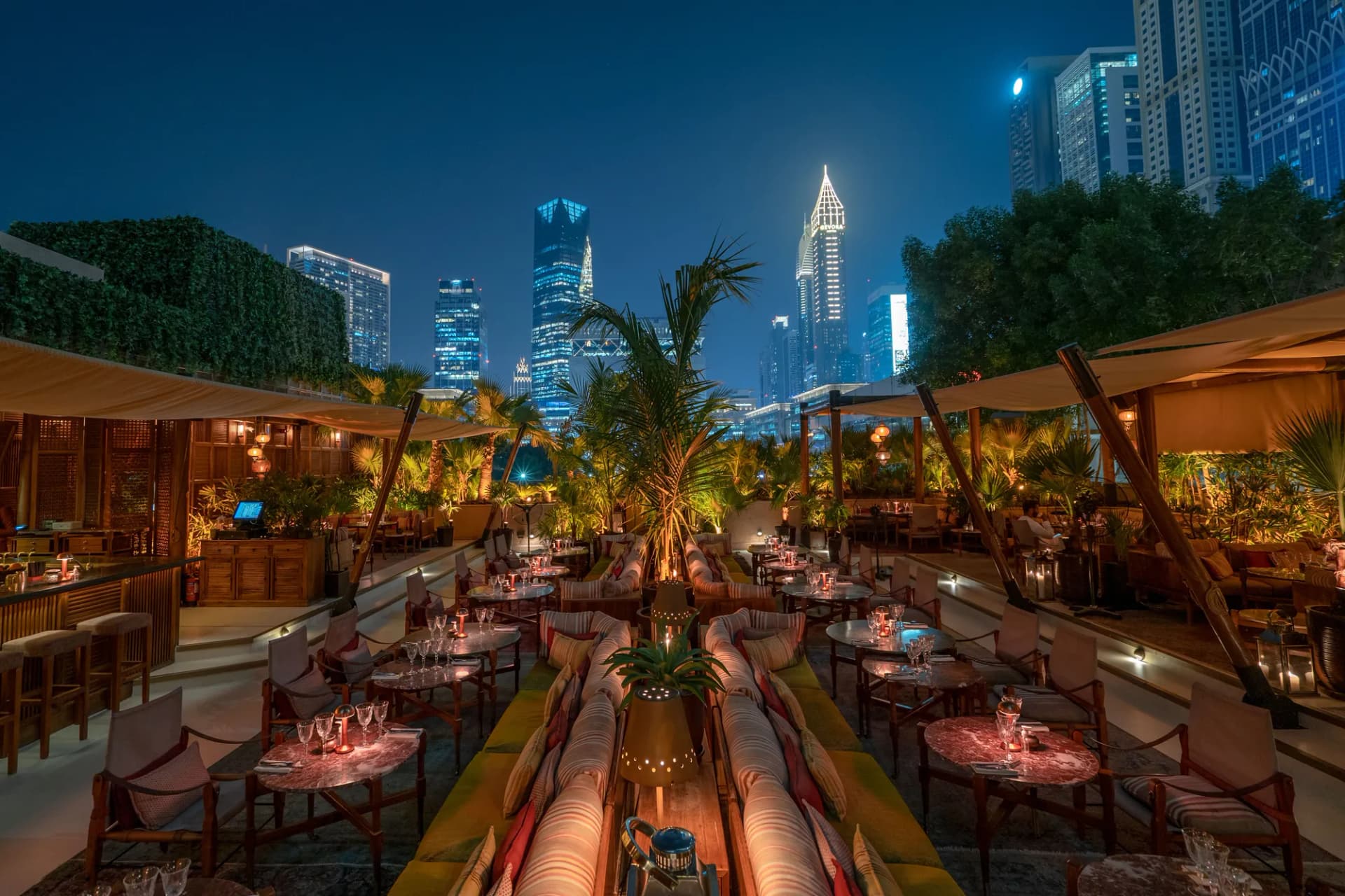 Ninive's terrace at night: striped sofas and low tables under palms, the DIFC towers lit up behind