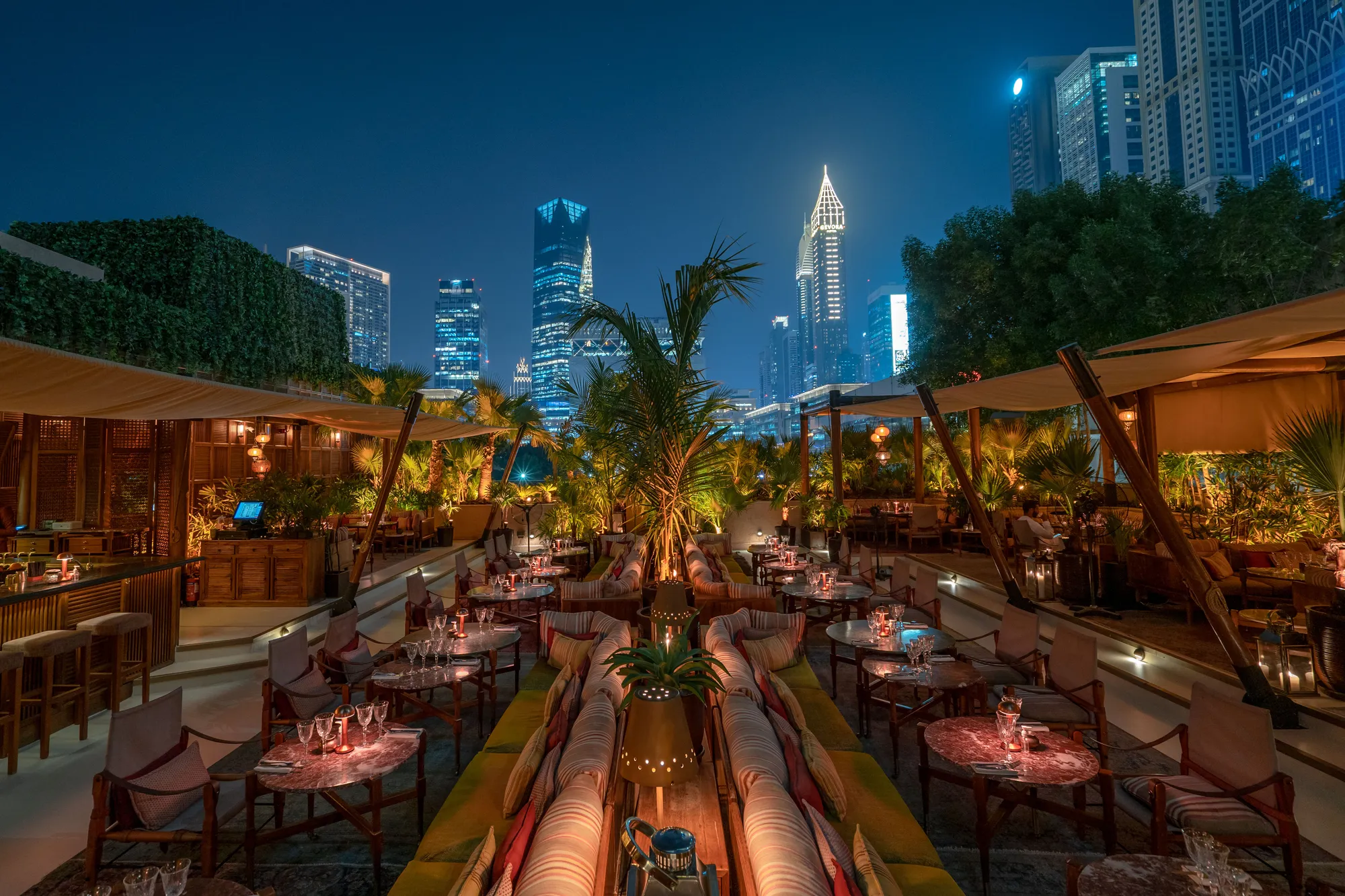 Ninive's terrace at night: striped sofas and low tables under palms, the DIFC towers lit up behind