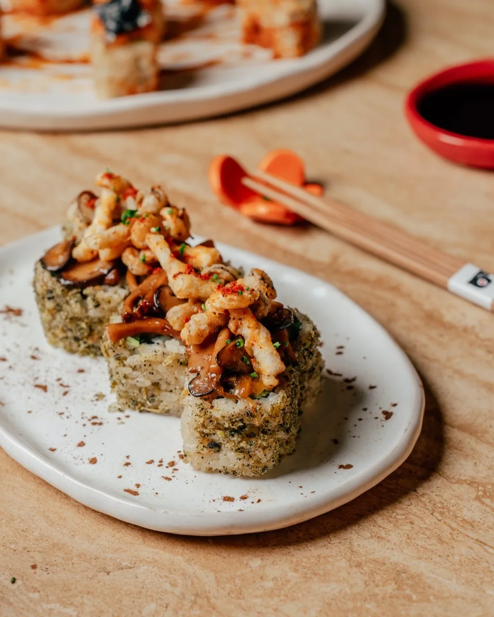 Maki pieces topped with mushrooms and crisp tempura, chopsticks and soy sauce behind