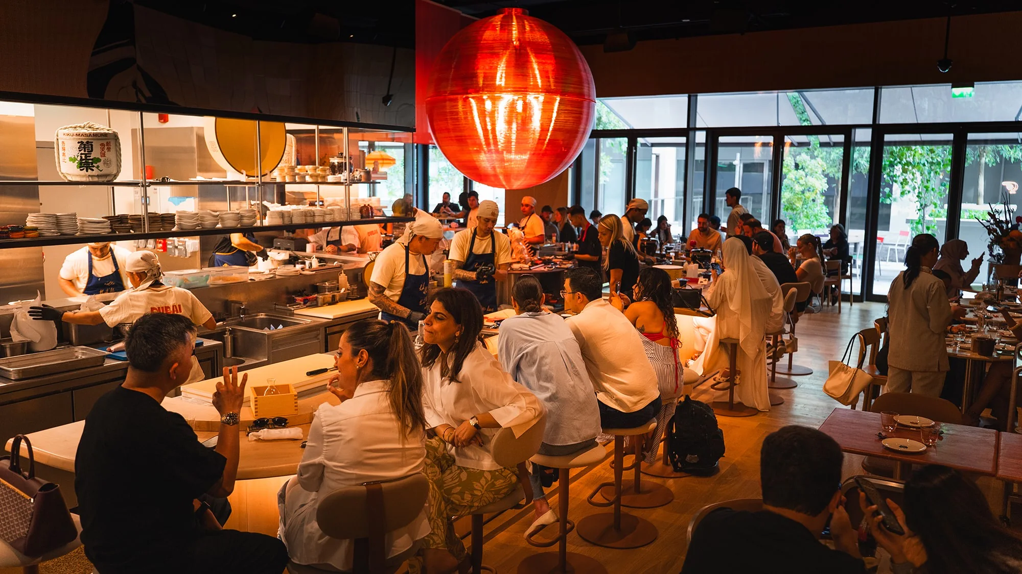 The packed dining room at lunch, chefs working the open counter beneath the giant red lantern