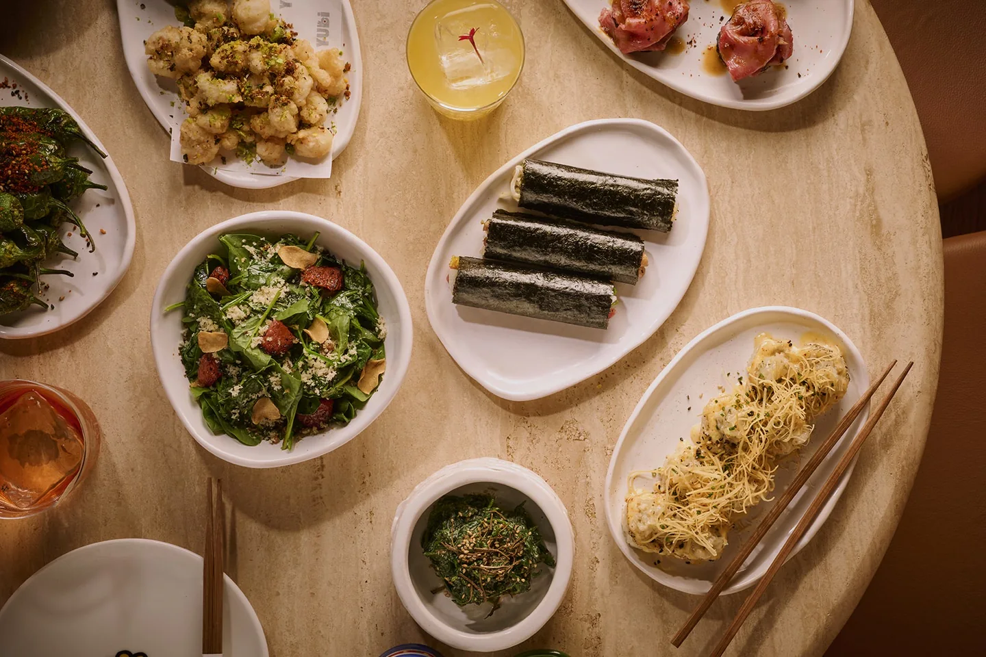 Overhead view of a round stone table set with handrolls, gyoza, salads, small plates and cocktails